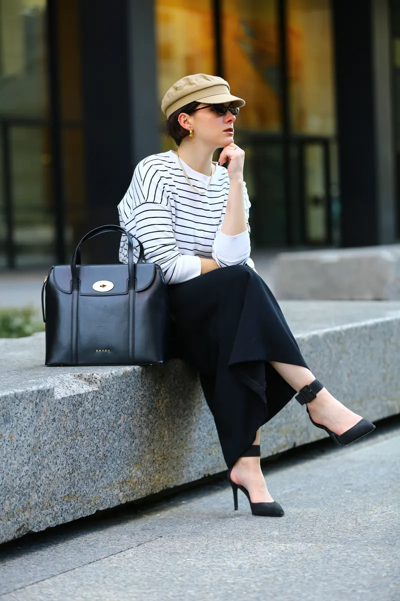 Woman in a striped top with a black bag, sitting on a ledge